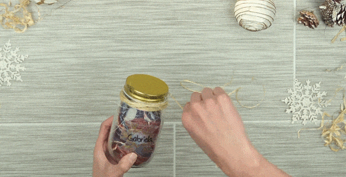 Manos de mujer atando un cordón alrededor de la tapa del frasco.

